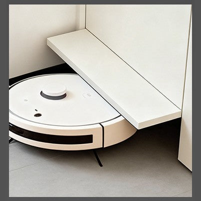 White robot vacuum passing under an opened cabinet base panel